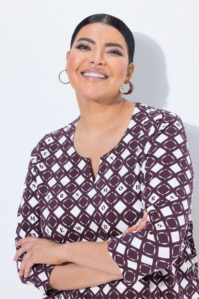 A smiling woman with dark hair pulled back wears the Ulla Popken Wine Print Blouse a patterned top with three-quarter sleeves. The top has a white base with a dark plum geometric diamond pattern.