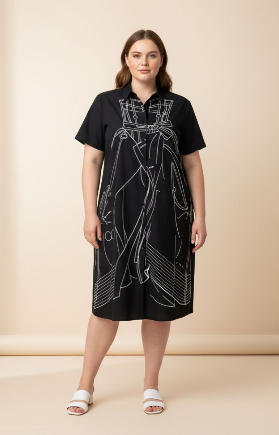 Woman wearing the Vera Dress in Black, a black dress with white line art design on a beige background
