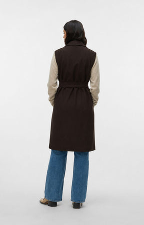 Model is wearing the Vero Moda Curve Fortuneaya Long Waistcoat in Brown, a long line waistcoat with a collar and lapels,tie belt closure, side pockets and a rich, deep chocolate brown shade. This image was created using AI.