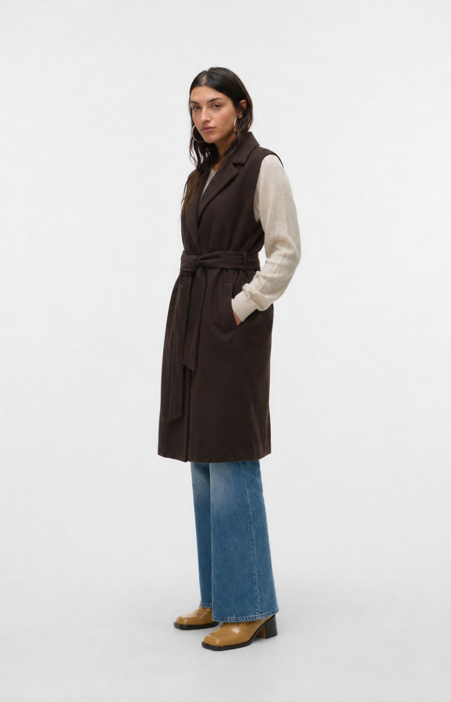 Model is wearing the Vero Moda Curve Fortuneaya Long Waistcoat in Brown, a long line waistcoat with a collar and lapels,tie belt closure, side pockets and a rich, deep chocolate brown shade. This image was created using AI.