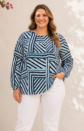 Woman wearing a blue and black patterned top with white pants against a neutral background