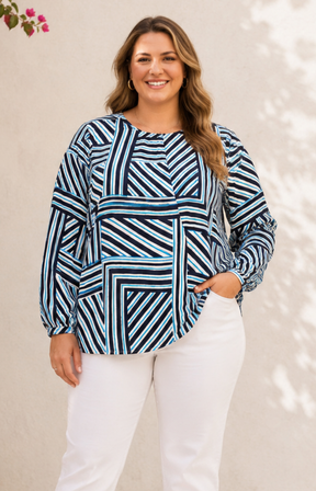 Woman wearing a blue and black patterned top with white pants against a neutral background