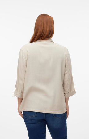 Woman wearing a beige blazer with 3/4 length sleeves and blue jeans on a white background