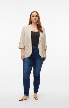 Woman wearing a beige open front blazer, black top, and blue jeans on a white background