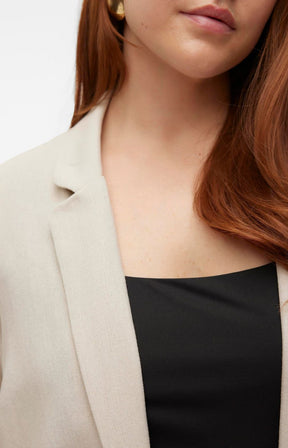 Close-up of a person wearing a beige blazer with collar and lapels over a black top.