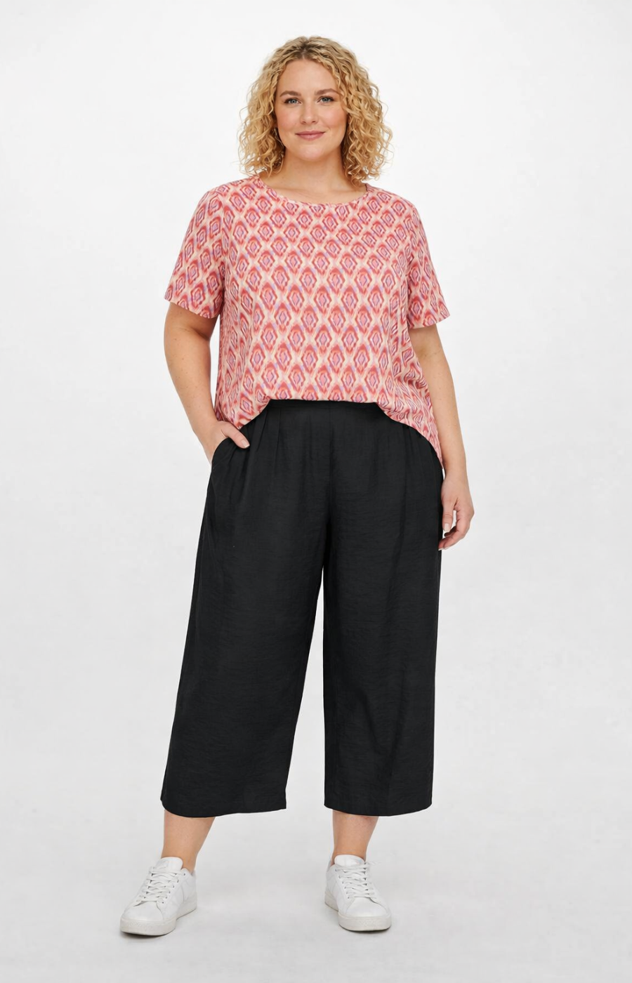 Woman wearing a pink patterned top and black wide-leg pants on a white background