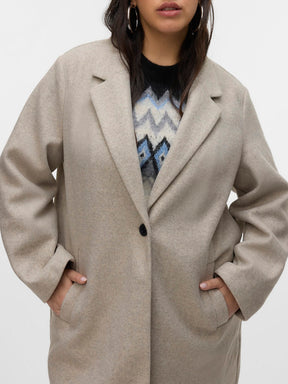 Person wearing a beige coat over a patterned sweater on a white background
