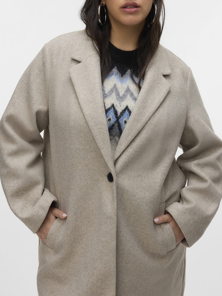 Person wearing a beige coat over a patterned sweater on a white background