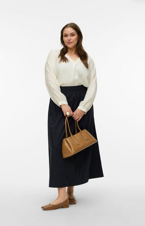 Woman wearing a white blouse with a V neckline and long sleeves, and black skirt holding a brown handbag on a white background