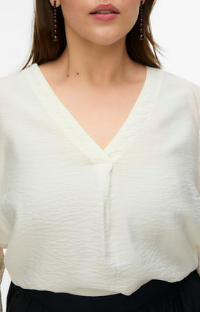 Close-up of a person wearing a white blouse with a V neckline and inverted pleate with a blurred background