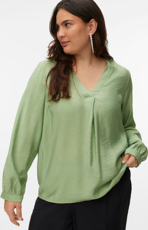 Woman wearing a green blouse with a V neckline, inverted pleat and long sleeves with buttoned cuffs with a plain background