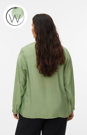 Woman wearing a green blouse with a V neckline, inverted pleat and long sleeves with buttoned cuffs with a plain background