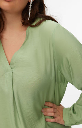 Green top with V neckline and long sleeves worn by a person on a white background