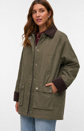 A woman wearing the Vero Moda Curve Wales Jacket in Grape Leaf,  an olive green jacket with dark brown collar, cuffs, and pocket trim, paired with blue jeans, against a plain white studio background. This image was created using AI.