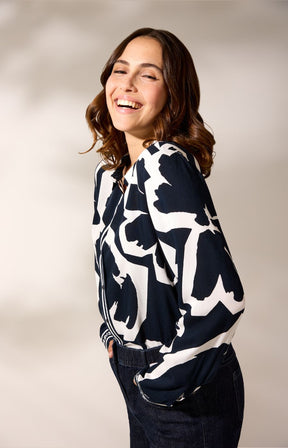 Woman wearing a Navy and white floral patterned shirt and dark jeans against a plain background