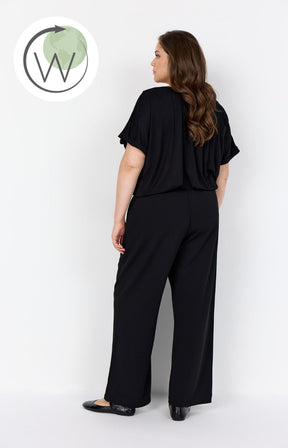 Woman wearing Wasabi Kufa Trousers in Black, They have a full length straight leg, elasticated waistband and wearing a black t-shirt