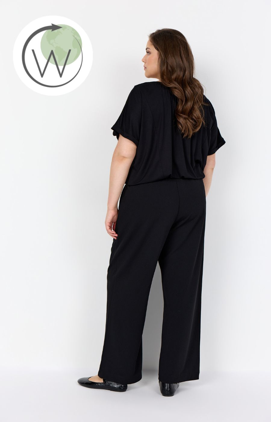 Woman wearing Wasabi Kufa Trousers in Black, They have a full length straight leg, elasticated waistband and wearing a black t-shirt