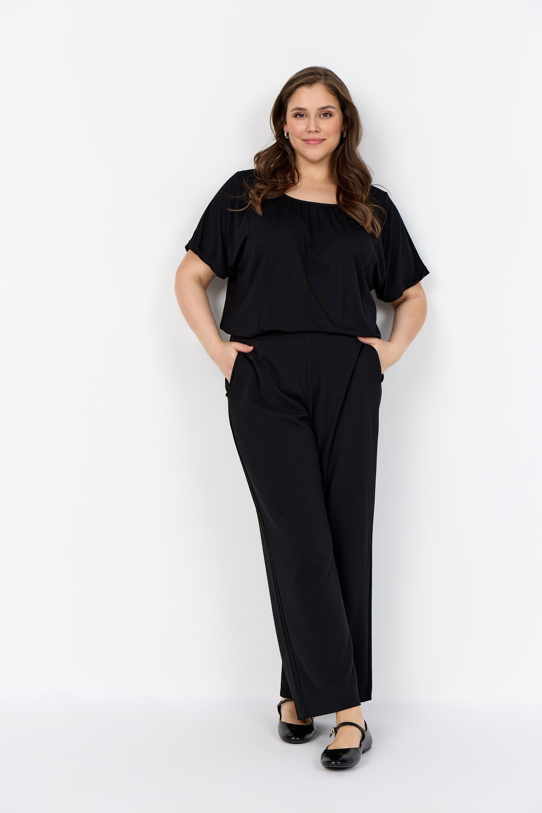 Woman wearing Wasabi Kufa Trousers in Black and a black t-Shirt. These trousers have a straight, full length leg and side pockets