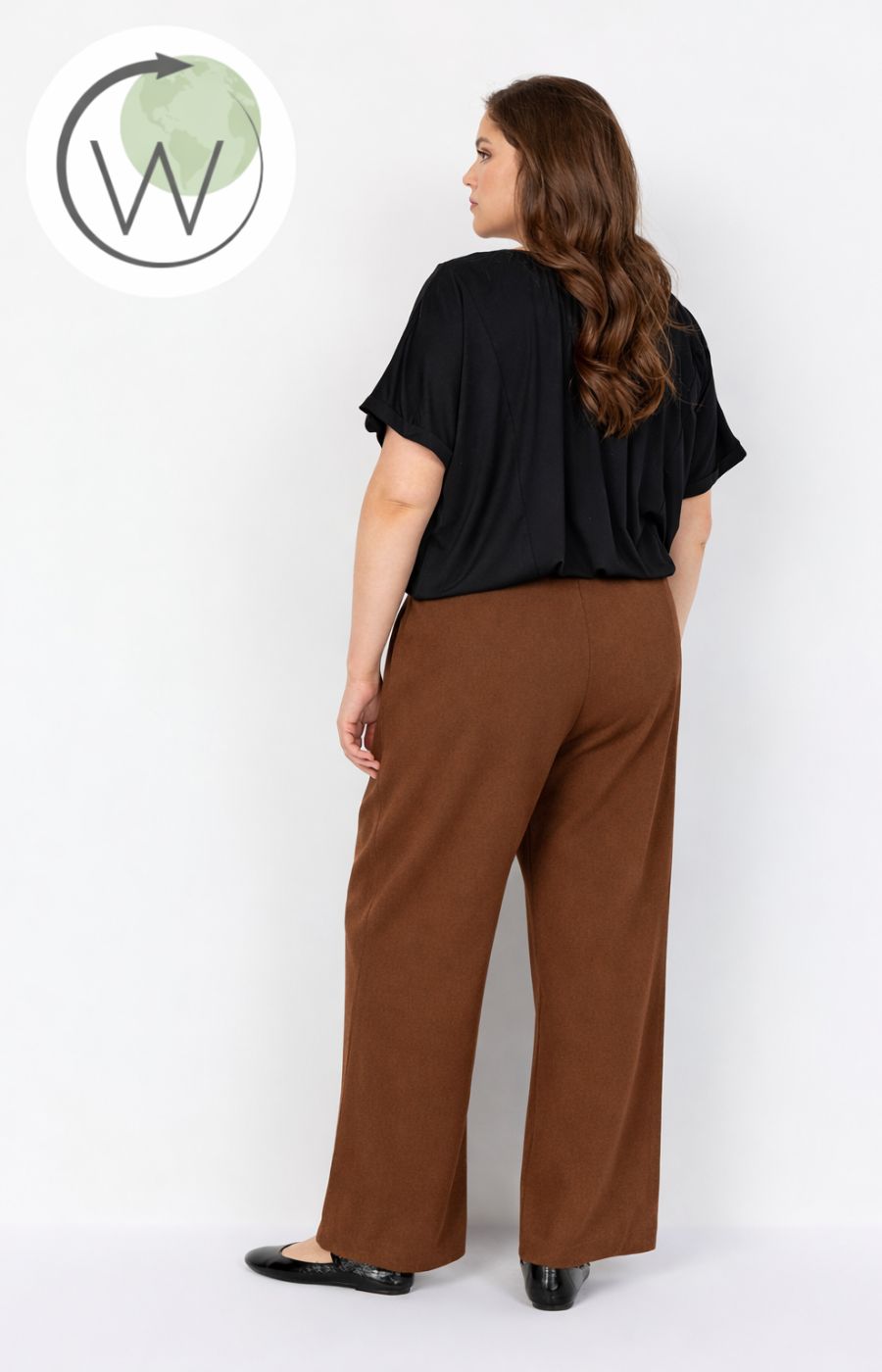 Woman wearing a black top and Wasabi Kufa Trousers, a full length, straight leg trouser in Brown on a white background