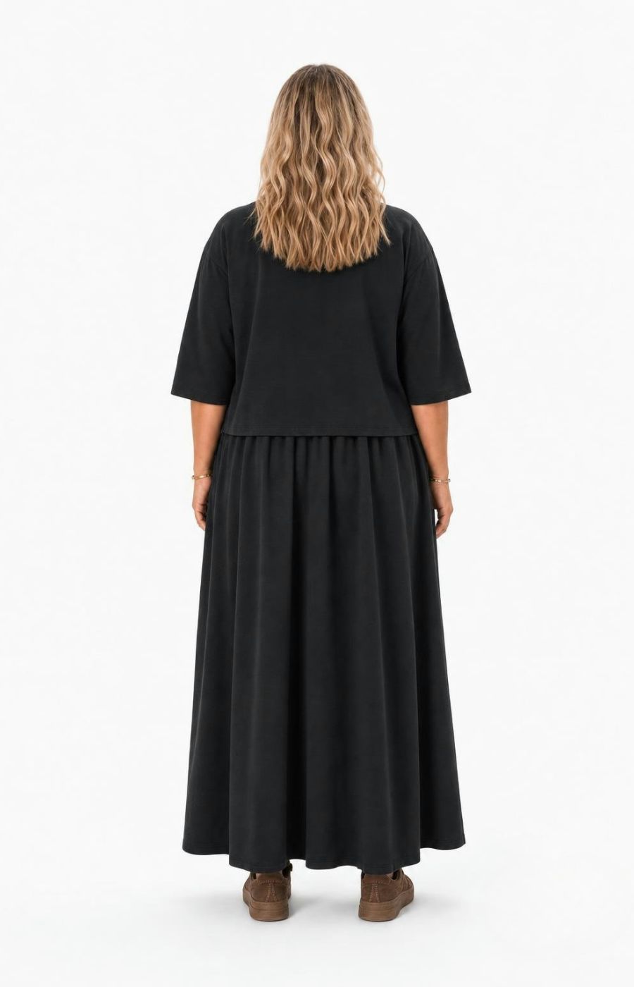 A woman viewed from the back wearing  the Wasabi Sabina Dress in Black, a black two-piece look outfit consisting of a short-sleeve top and a long flared skirt, paired with brown shoes, against a plain white studio background. This image has been created using AI.