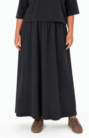 A person wearing the Wasabi Sabina Dress in Black, and brown suede sneakers, shown against a plain white studio background. This image has been created using AI.
