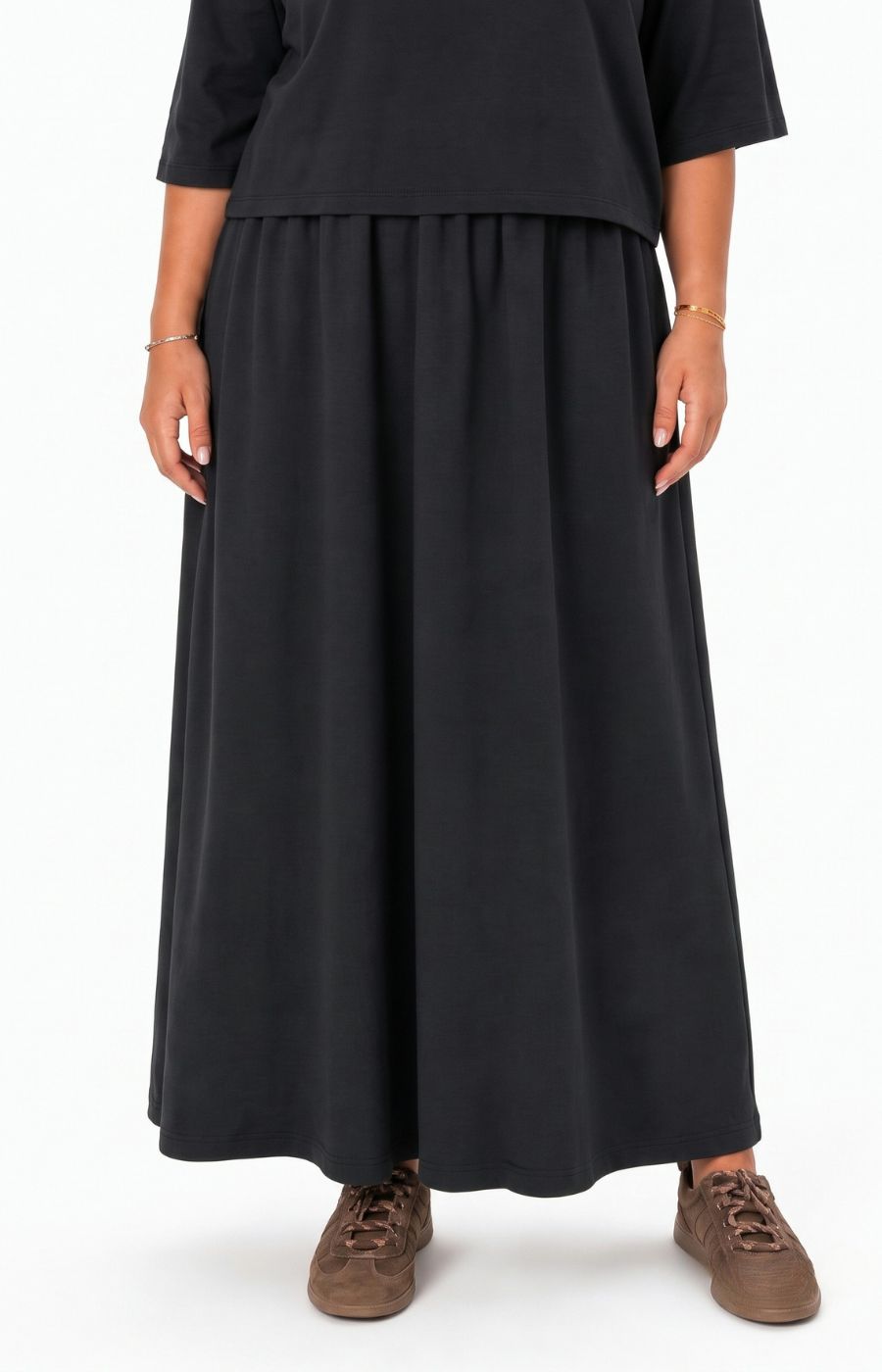 A person wearing the Wasabi Sabina Dress in Black, and brown suede sneakers, shown against a plain white studio background. This image has been created using AI.