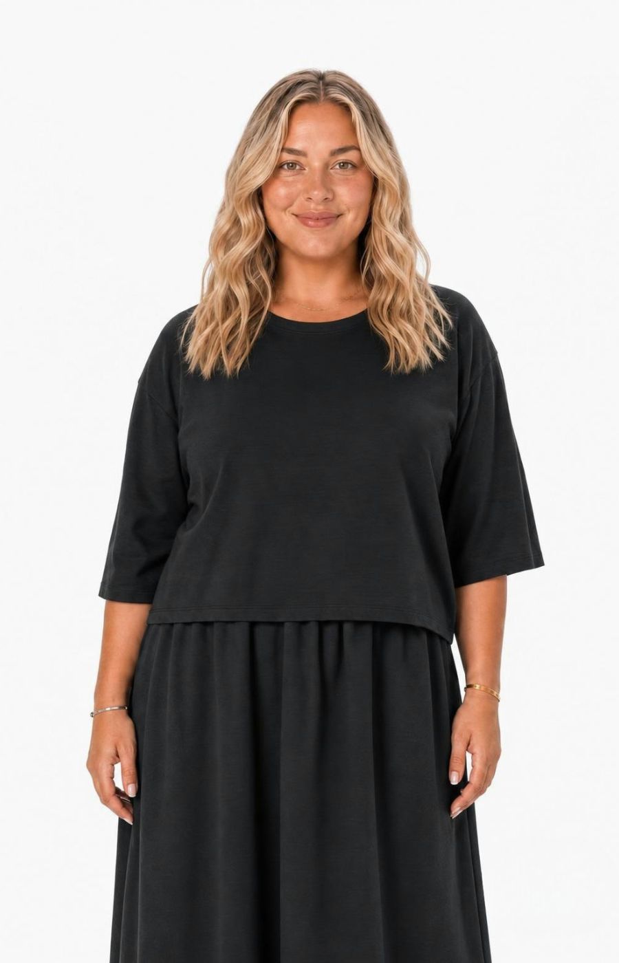A woman with blonde wavy hair wearing the Wasabi Sabina Dress in Black, a black two-piece look outfit, standing against a plain white background. This image has been created using AI.