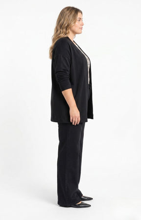 A woman stands in side profile wearing the Wasabi Sabina Pocket Cardigan in Black, a black cardigan, black pants, and black flats against a plain white studio background. This image has been created using AI