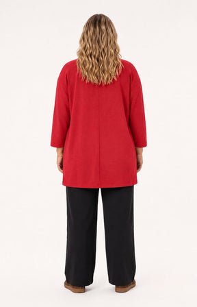 A woman viewed from the back wearing the Wasabi Sabina Pocket Cardigan in Red, a bright red long-sleeve tunic-style top and black wide-leg pants, standing against a plain light background. This image was created using Ai