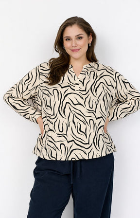 Woman wearing Wasabi Saliha Blouse in Cream, a blouse with a V neck, long sleeves and ans all over animal print and navy pants against a white background