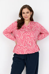 Woman wearing Wasabi Saliha Blouse in Pink, a blouse with long sleeves, a V neckline and an elasticated waist and navy pants against a white background