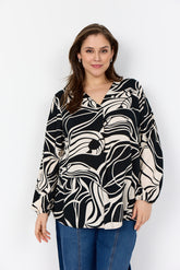 Woman wearing the Wasabi Samena Blouse in Black, a V neck, long sleeves blouse with an all over print with blue jeans on a white background