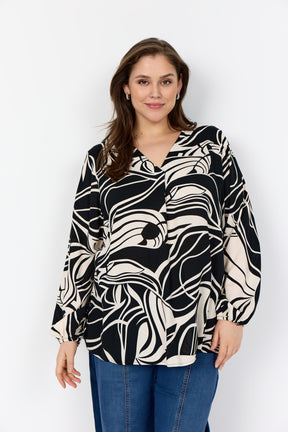 Woman wearing the Wasabi Samena Blouse in Black, a V neck, long sleeves blouse with an all over print with blue jeans on a white background