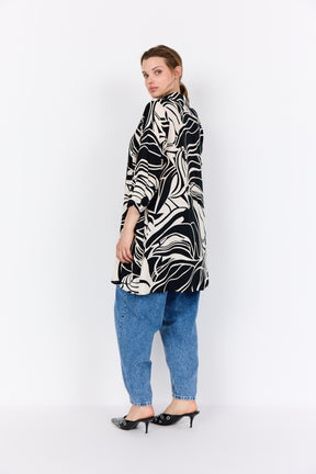 Woman wearing Wasabi Samena Tunic in Black, a long line tunic with 3/4 length sleeves and an all over print with blue jeans on a white background
