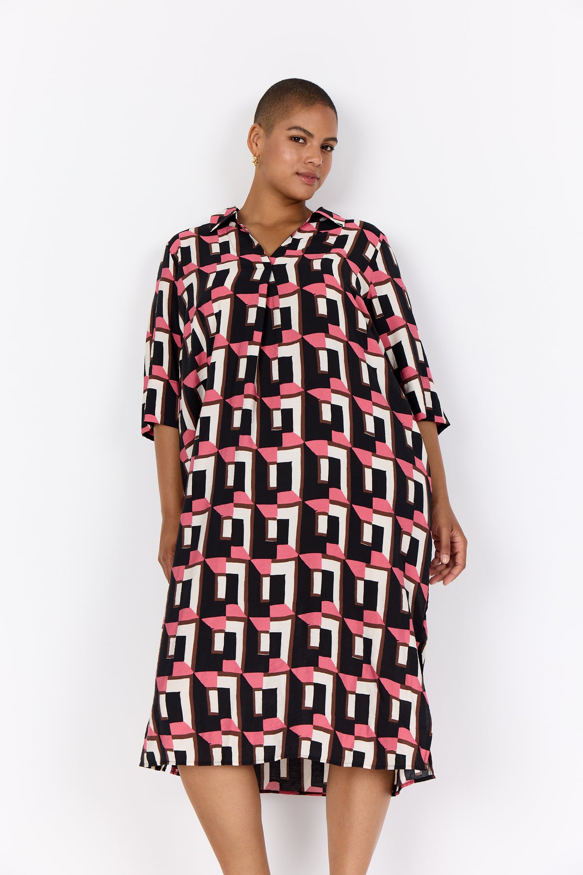 Woman wearing Wasabi Sarena Dress in Pink on a white background, a V neck dress with 1/2 sleeves, a midi length with an all over geometric print in pink, black and white