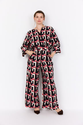Wasabi Sarena Trousers in Pink, a wide leg trouser with an all over geometric print in pink, black and white, worn with the matching shirt 
