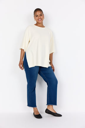 Woman wearing Wasabi Sikka Jumper in Cream, an oversized fit with side slits, 1/2 sleeves and a round neckline with blue jeans on a white background