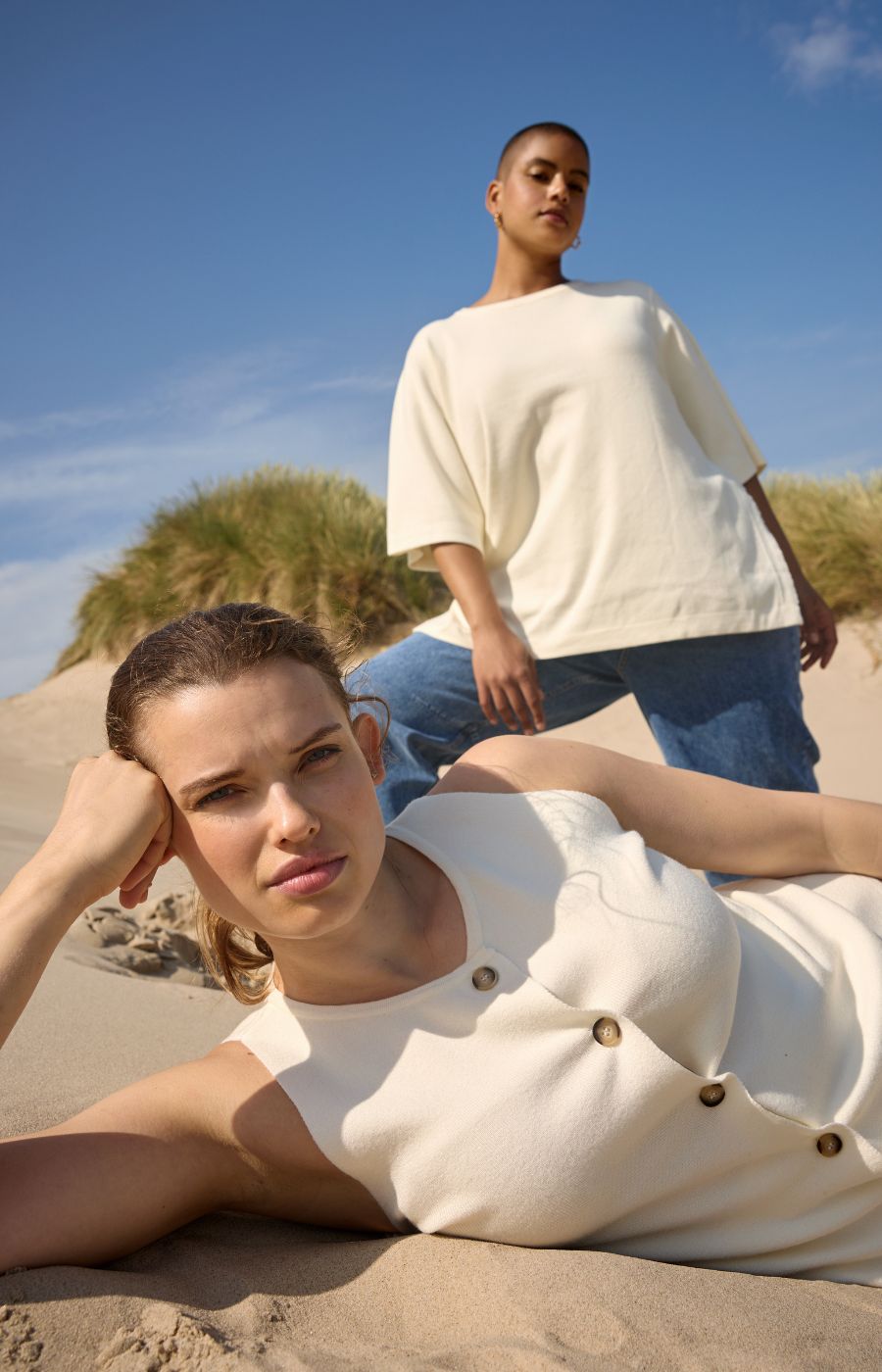Two people on a beach, one sitting and one standing, wearing Wasabi Sikka tops.