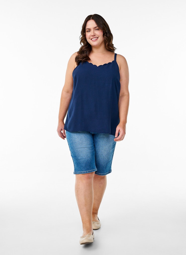 Woman wearing a navy blue sleeveless top and denim shorts on a white background