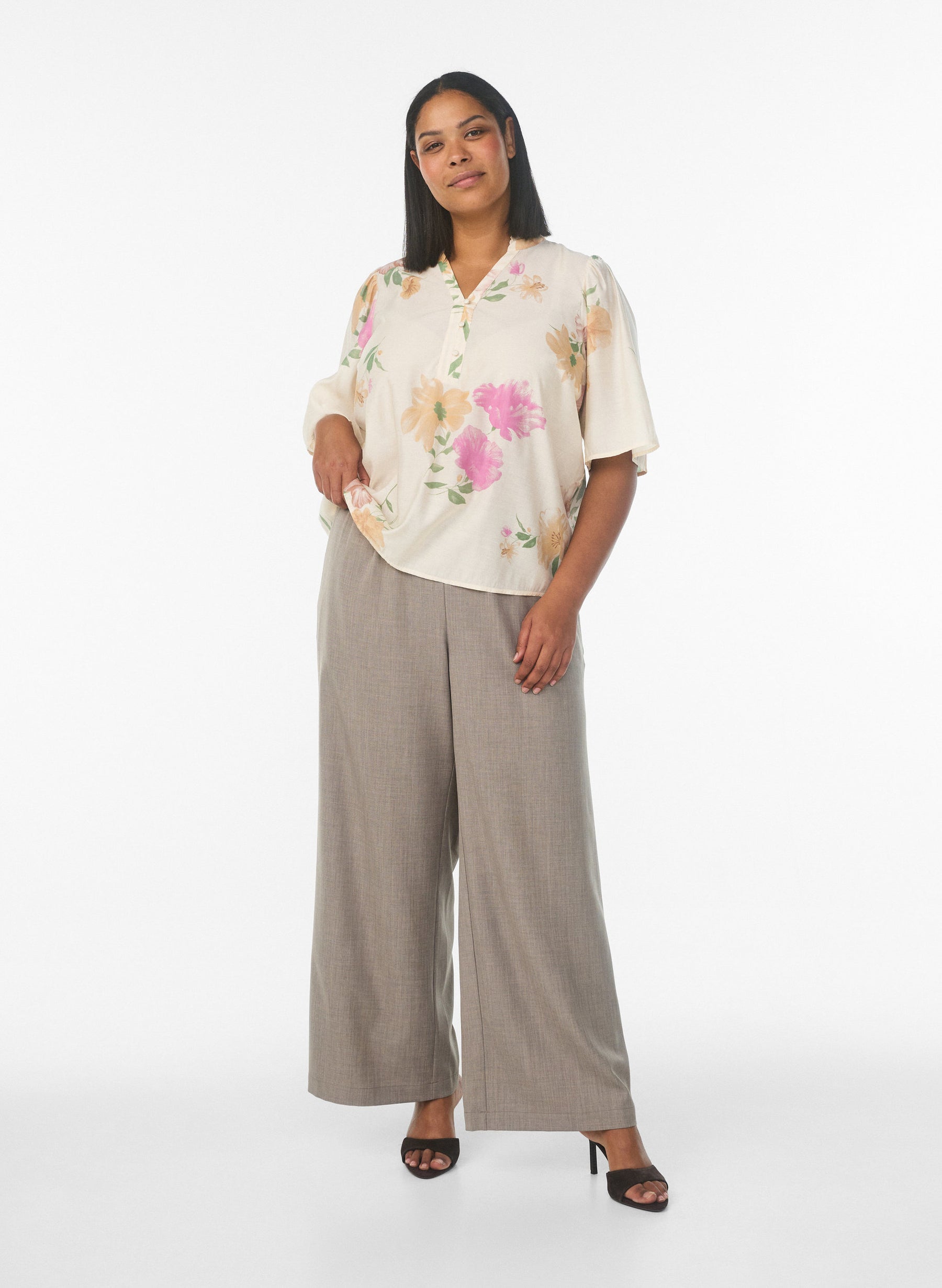 Woman wearing a floral blouse and wide-leg pants on a white background