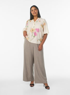 Woman wearing a floral blouse and wide-leg pants on a white background