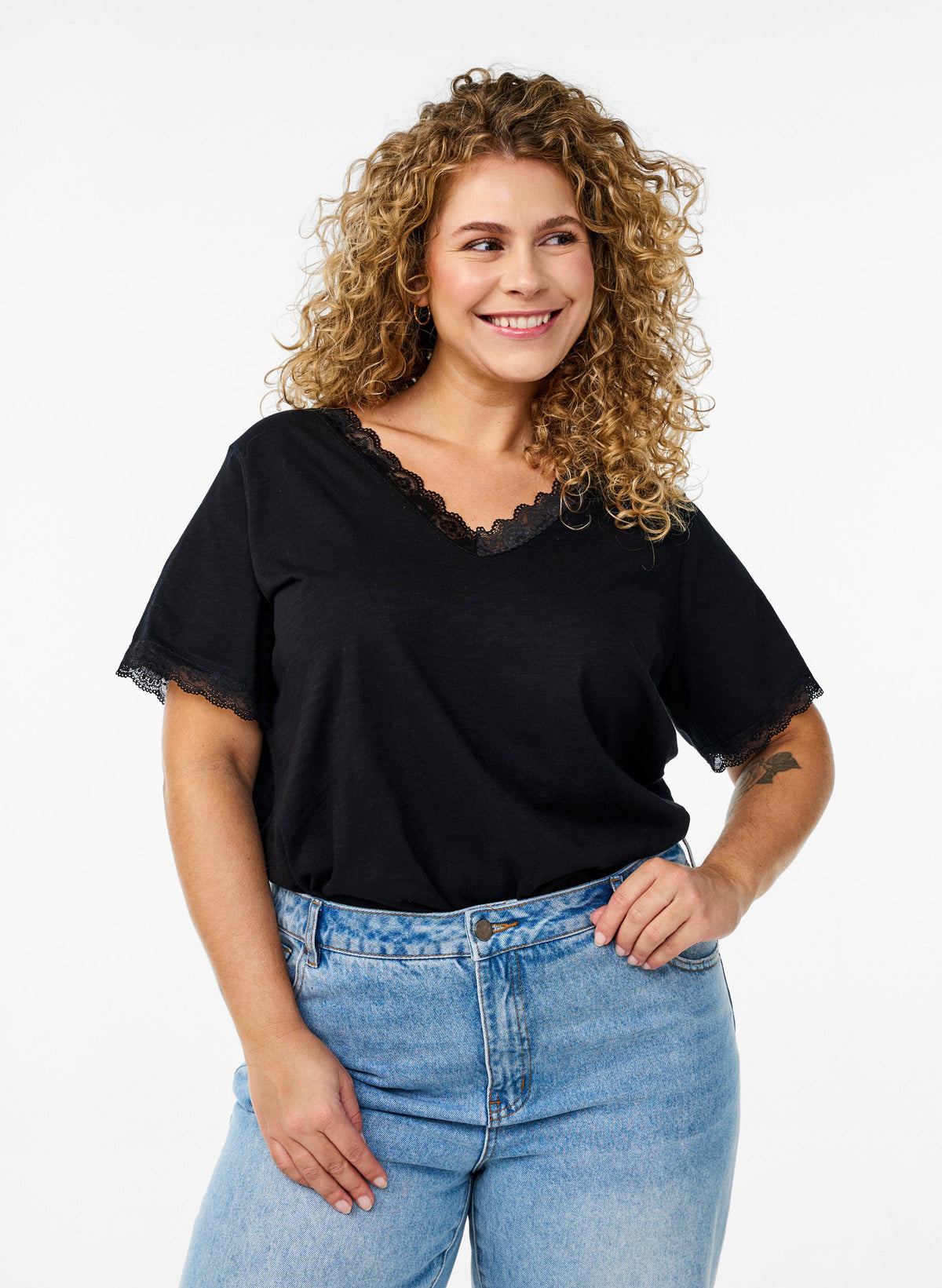 Zizzi Kamia T-Shirt in Black, A V neck, short sleeve top, neck and sleeves both with lace edging, worn with jeans 