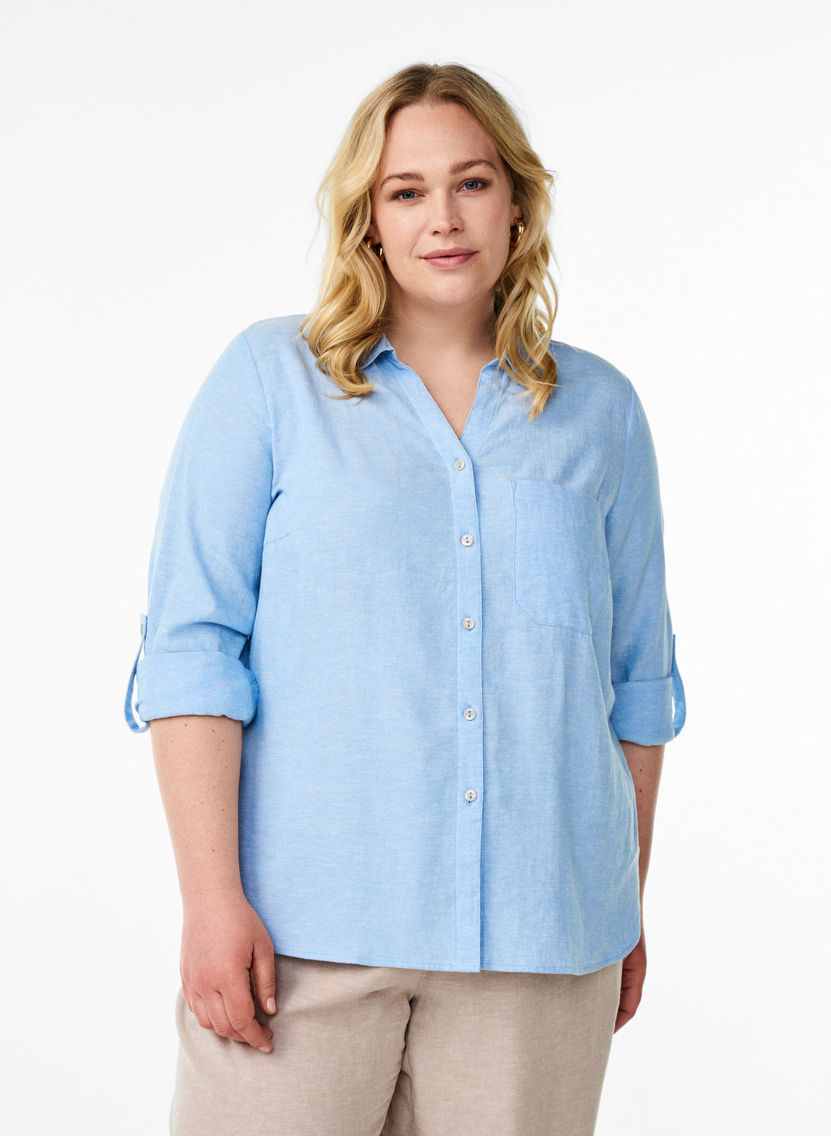 Woman wearing the Zizzi Lina Shirt in Blue, a v neck collared shirt with a button up front, a breast pocket and long sleeves turned up on a white background