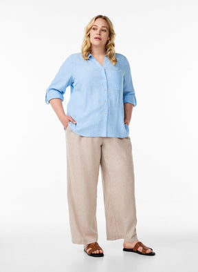 Woman wearing the Zizzi Lina Shirt in Blue and beige pants on a white background