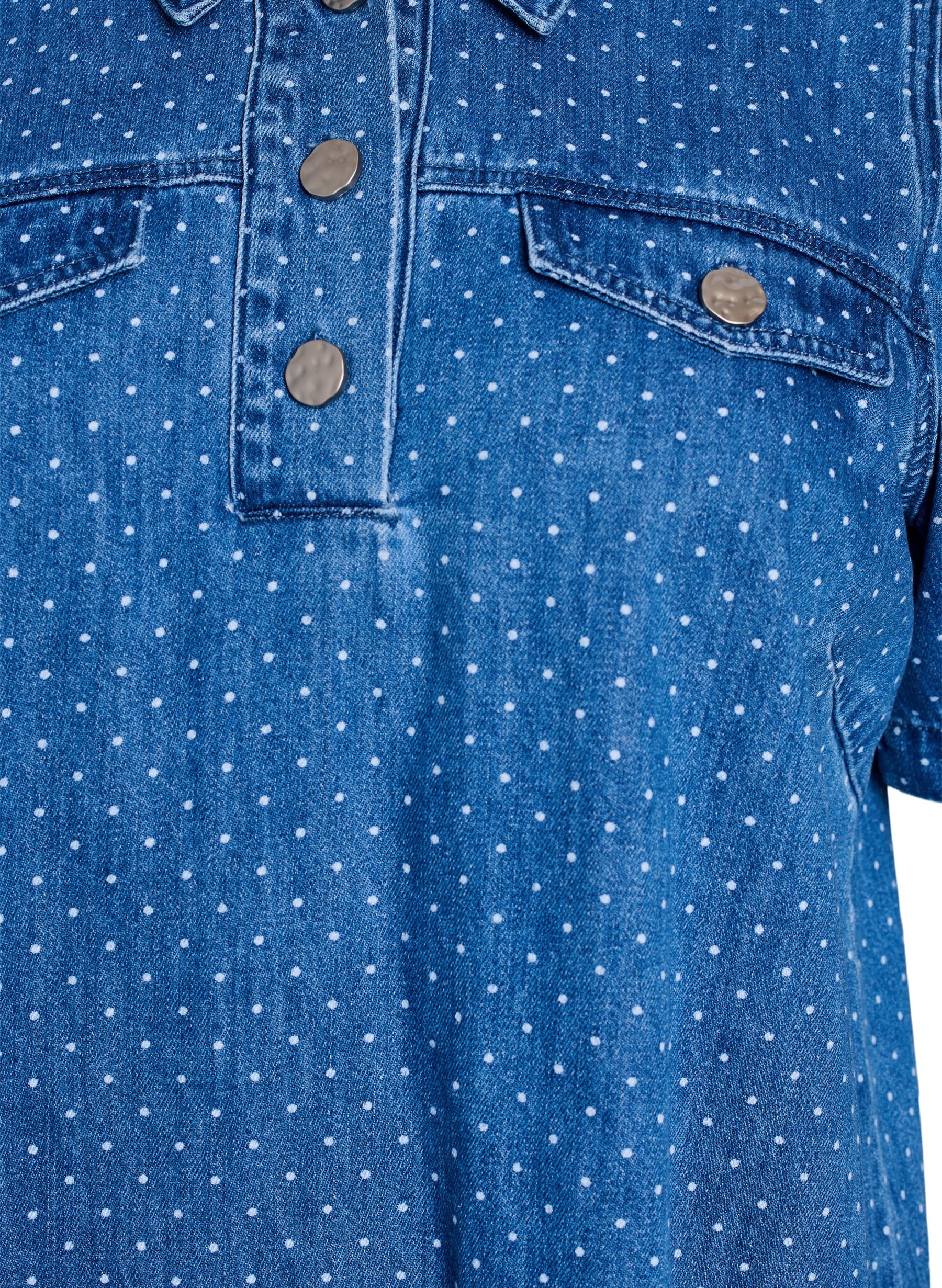 Close-up of the Zizzi Misha Denim Dress, a blue denim shirt with white polka dots and button details on faux pockets.