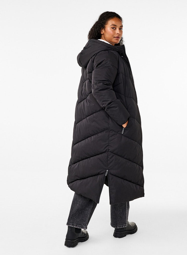 Person wearing a long black puffer coat on a white background