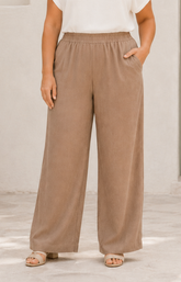 Person wearing brown wide-leg pants and a white top against a neutral background