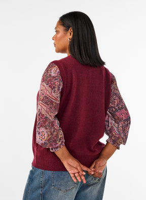 A woman shown from the back wearing the Zizzi Vista Waistcoat in Windsor Wine a burgundy knit sweater vest with patterned puff sleeves, paired with blue jeans, against a plain white studio background. 