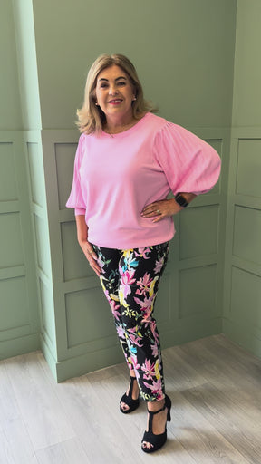 A video of a curvy woman wearing a pink 3/4 sleeve fine knit top and black trousers with a floral print