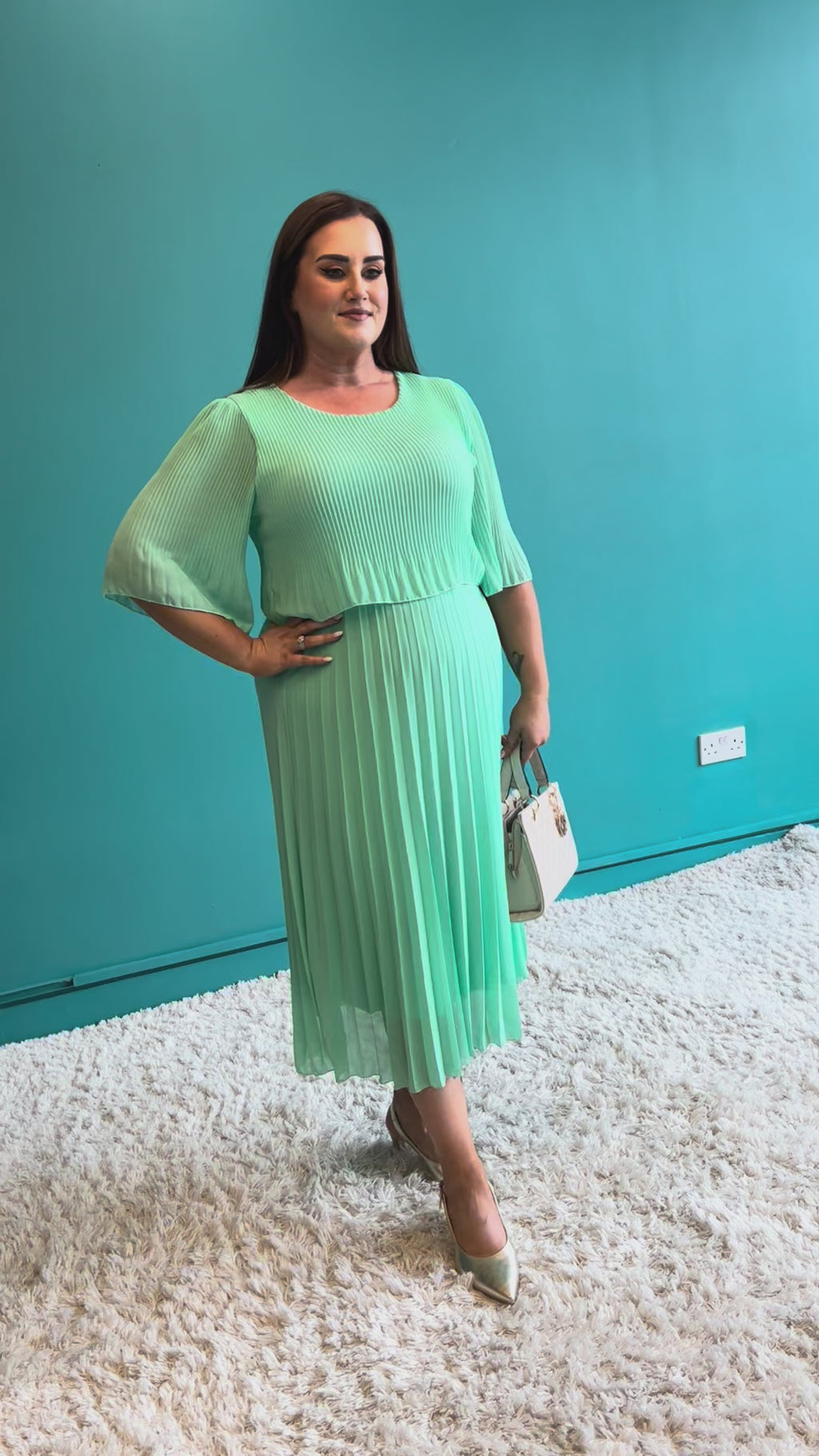 Woman wearing a light green pleated dress on a teal background